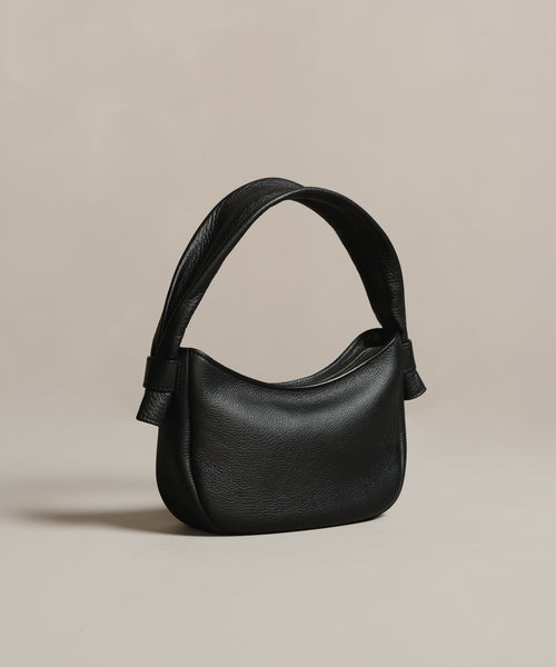The Loren Shoulder Bag is crafted from soft pebbled leather with a curved top, wide strap, and subtle textured finish, shown against a neutral beige background.