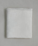 The Dusk Linen Flat Sheet, in crisp white, lies neatly folded on a light gray surface. Its soft, smooth fabric and minimal texture offer understated elegance—ideal for those who love luxurious bedding.