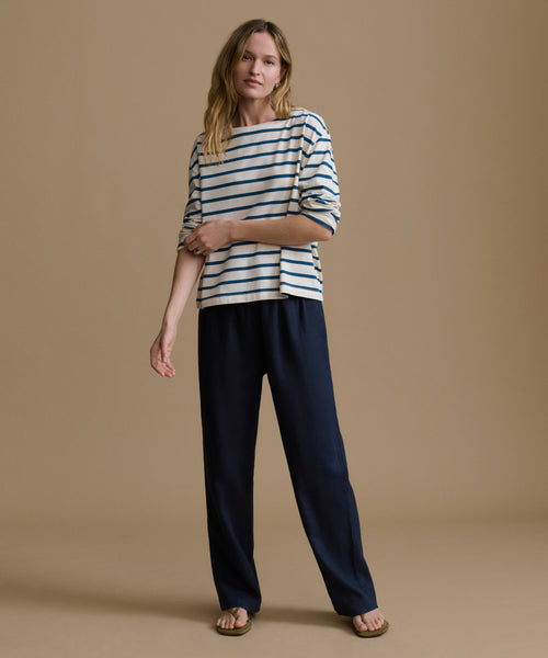 Woman wearing a striped shirt and navy pants on a brown background