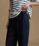 Woman wearing a striped shirt and navy pants on a brown background