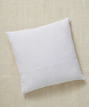 A Linen Pillow in square white design with a feather down insert rests atop a textured beige fabric surface, captured from an overhead angle.
