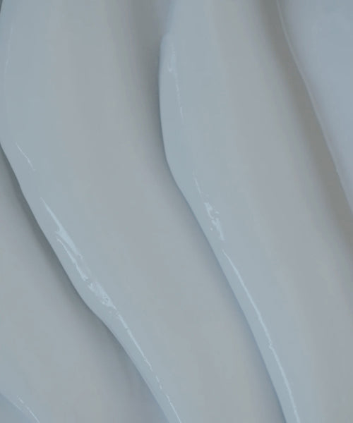 Close-up of Luminous Body Lotion’s smooth, glossy white surface with gentle, wavy ridges running diagonally for a soft, flowing texture.