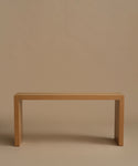 A minimalist light oak wood entry table with a rectangular top and blocky legs, photographed against a solid warm beige background.