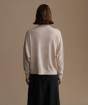Woman wearing a beige cashmere sweater and dark pants against a brown background