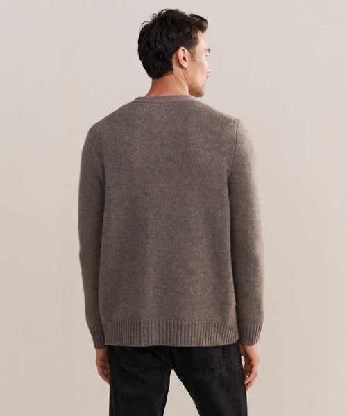 A man stands with his back to the camera, wearing a gray Mens Cashmere Cardigan and black pants against a plain light background.