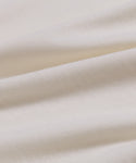 Close-up of soft, ivory-colored fabric from the Merino Tee. Gentle folds and a smooth, finely woven surface showcase the tee’s elevated basic style and subtle shadows.
