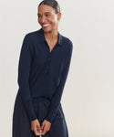 A dark-haired woman stands smiling against a plain light background, wearing the navy Grayson Pullover with matching bottoms and her hands clasped in front.