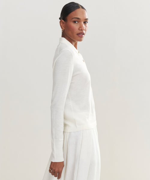 A woman with dark hair pulled back wears a long-sleeve, white Grayson Pullover and matching skirt, standing sideways and looking at the camera against a plain light background.