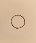 The Merit Emerald Cut Bracelet, featuring a small rectangular clasp, is elegantly arranged in a circle on a neutral beige background, highlighting the refined beauty of fine jewelry.