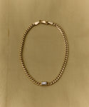 The Merit Emerald Cut Bracelet is a fine gold jewelry piece featuring a rectangular emerald-cut gemstone at its center, elegantly showcased on a light beige fabric background.