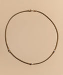 The Merit Round Cut Diamond Necklace features four evenly spaced round cut diamonds set in 14k gold, shown on a simple beige background—an elegant piece inspired by Jenni Kayne jewelry.