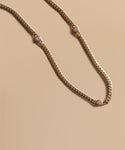 The Merit Round Cut Diamond Necklace by Jenni Kayne features three evenly spaced round diamonds set in 14k gold, elegantly displayed on a smooth beige background.
