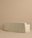 The Miramar Sofa, shown from the back against a plain light brown background, features a beige slipcover, clean lines, soft edges, and the inviting comfort of Belgian linen in a minimalistic design.
