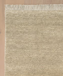 A close-up of the Mojave Jute Rug, featuring beige tones, horizontal lines, and fringed edges on a light wooden floor. Only part of the rug is visible, highlighting its handcrafted weave and detailed fringe.