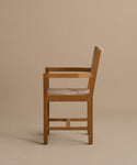 The Outdoor Montecito Dining Arm Chair Frame is shown in profile against a beige background, featuring clean lines, a modern design, and corrosion-resistant materials for lasting durability. Beige cushioned seat and backrest included.