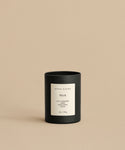 A Musk Glass Candle with a white label reading jenni kayne, Musk, Spicy Cardamom, Sandalwood, Orchid, 10oz / 283g sits on a beige surface. This hand-poured coconut soy wax candle is made in Los Angeles and matches the background.