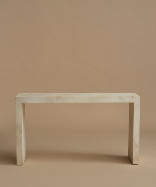 A minimalist console table made of light beige parchment with subtle white veining, set against a solid warm beige background.