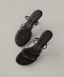 The Eve Heeled Sandal, crafted in black nappa leather with thin crisscross straps and an open toe, is displayed on a light, neutral surface.