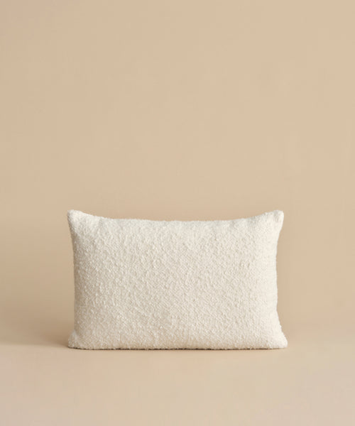 The Nell Boucle Lumbar Pillow, featuring a textured ivory finish and rectangular shape, sits upright against a plain beige background.
