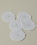 Five Reusable Cotton Rounds are arranged on a light beige surface, slightly overlapping. Each white, round pad features central oval stitching, making them perfect for elevating your cleansing routine.