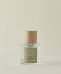 Against a beige backdrop, the clear glass Cuir Rose Eau De Parfum bottle—with a light wood-grain cap and green label—showcases its clean fragrance, blending floral and woody notes.