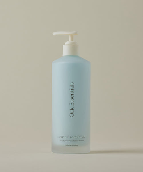 A blue bottle of Luminous Body Lotion with a white pump dispenser sits on a beige surface, featuring a modern label that hints at nourishing ingredients for radiant skin.