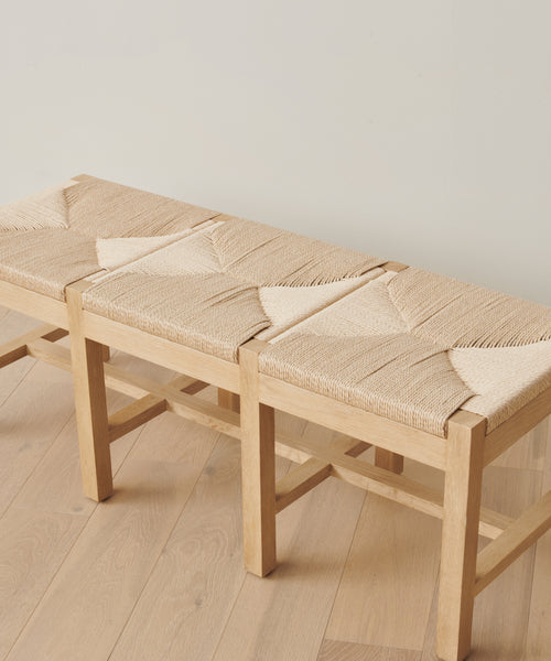 The Montecito Bench features three seats, each with a woven Danish paper cord pattern. Crafted from white oak, it brings natural elegance to any space when placed on a light wood floor against an off-white wall.