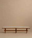The Outdoor Garden Dining Bench features a minimalist solid teak frame, simple lines, and a light beige Tempotest fabric cushion. Set against a plain beige background, this sturdy bench offers comfort and style for any outdoor space.