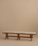 The Outdoor Garden Dining Bench features a long solid teak frame, X-shaped legs, and a Tempotest fabric cushion—ideal for outdoor dining—shown against a plain beige background.