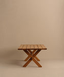 The Outdoor Garden Dining Table features a slatted rectangular teak top and crossed legs, shown against a plain beige background.