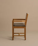 The Outdoor Montecito Dining Arm Chair, crafted from solid teak with a straight back and square frame, features cushioned seat and backrest in light gray fabric, shown in a side view against a plain beige background.
