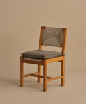 The Outdoor Montecito Dining Chair features a modern design with a cushioned gray seat, woven ECOLENE backrest, and solid teak frame. Set against a plain beige background, its clean lines and simple style create an elegant outdoor seating option.