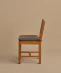 The Outdoor Montecito Dining Chair, made of solid teak with a gray cushioned seat and straight backrest, is shown in profile against a plain beige background.