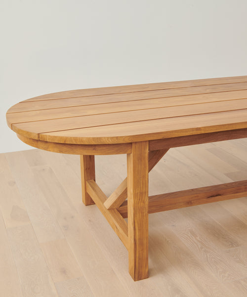 The Outdoor Montecito Oval Dining Table sits against a white wall, perfect as an elegant centerpiece for outdoor dining, whether for lively gatherings or peaceful moments.