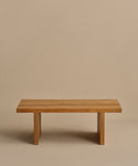 The Outdoor Vista Coffee Table, a minimalist teak piece with a rectangular top and two wide, flat legs, is shown against a plain beige background.