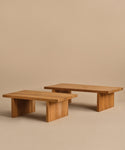 Two low, rectangular Outdoor Vista Coffee Tables with simple, modern design feature thick tops and sturdy block legs. Placed side by side on a beige floor and background, they add style to any outdoor space.