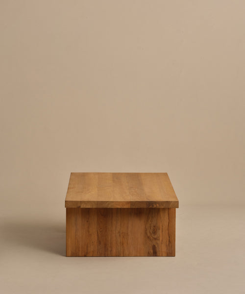 The Outdoor Vista Coffee Table features a minimalist rectangular teak design with a smooth flat top, showcased against a plain beige background.