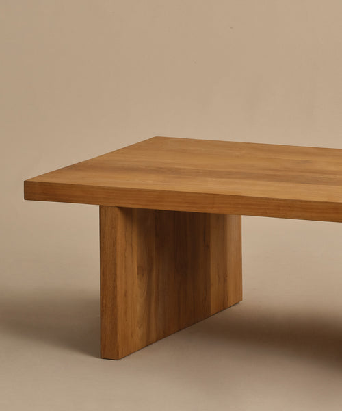 The Outdoor Vista Coffee Table features a minimalist teak design with a thick rectangular top and sturdy wide legs, displayed against a neutral beige background.