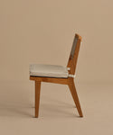 The Outdoor Vista Dining Chair is a minimalist, modern piece crafted from solid teak with a woven backrest and light beige cushion, displayed in profile against a plain beige background.