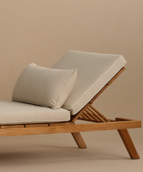 The Outdoor Vista Lounge Chair boasts a minimalist teak frame, angled legs, beige cushions, and a matching pillow, all set against a plain beige background—highlighting its sleek design and durable appeal for outdoor living.