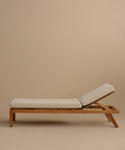 The Outdoor Vista Lounge Chair features a teak frame and light beige cushions on the seat and backrest, set against a plain beige background—ideal for anyone seeking durable outdoor furniture.