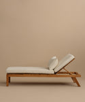 The Outdoor Vista Lounge Chair features a teak frame, white cushions, and adjustable backrest, offering stylish and durable outdoor seating. Shown against a plain beige background.