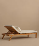 The Outdoor Vista Lounge Chair features a durable teak frame, white cushions, and an adjustable backrest, set against a plain beige background.