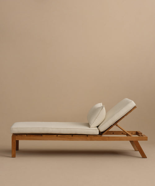 The Outdoor Vista Lounge Chair features a teak frame, white cushions, and adjustable backrest, offering stylish and durable outdoor seating. Shown against a plain beige background.