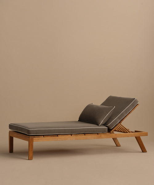 The Outdoor Vista Lounge Chair features a modern teak frame, gray cushions, and a matching pillow. Its angled backrest ensures comfort, making it the perfect choice for stylish outdoor relaxation against any neutral backdrop.