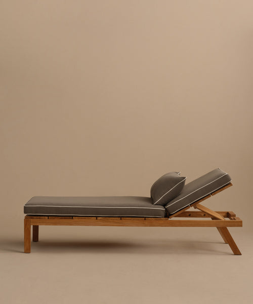 The Outdoor Vista Lounge Chair, crafted from teak with angled legs and gray cushioned seat and backrest, is displayed against a plain beige background.