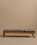 The Outdoor Vista Lounge Chair is a minimalist wooden daybed with two gray cushions, set against a plain beige background. Its simple, modern form and slightly elevated side are inspired by the timeless outdoor lounge chair design.