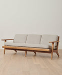 A modern wooden sofa with light beige cushions and three seats on a light wood floor against a white wall—perfectly protected by the Outdoor Vista Sofa Cover for stylish patio furniture care.