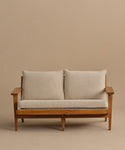 The Outdoor Vista Sofa features a wooden frame, light beige cushions, and two large back pillows, displayed against a plain beige background.