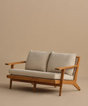 The Outdoor Vista Sofa features angled armrests and light beige Tempotest fabric cushions, crafted in modern teak and displayed against a plain beige background.